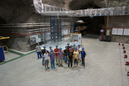 Fig. 1: Students and researchers from CUHK and HKU at the underground Daya Bay Far Experimental Hall. A full size model of an anti-neutrino detector is shown at the background.