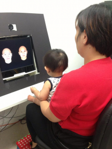 A HKU baby scientist sits on her mother's lap and watches visual figures displayed on the monitor while HKU researchers monitor their eye movements to decode their understanding and preference of the world.
